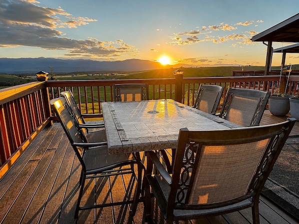 Une terrasse avec une table et des chaises, offrant une vue sur un paysage de montagnes et un coucher de soleil.