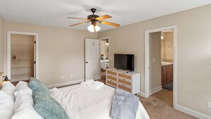 Ein Schlafzimmer mit Bett, Deckenventilator, Fernseher, Kommode und begehbarem Kleiderschrank.