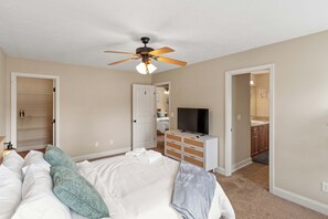 Un dormitorio con cama, ventilador de techo, televisión, cómoda y vestidor.