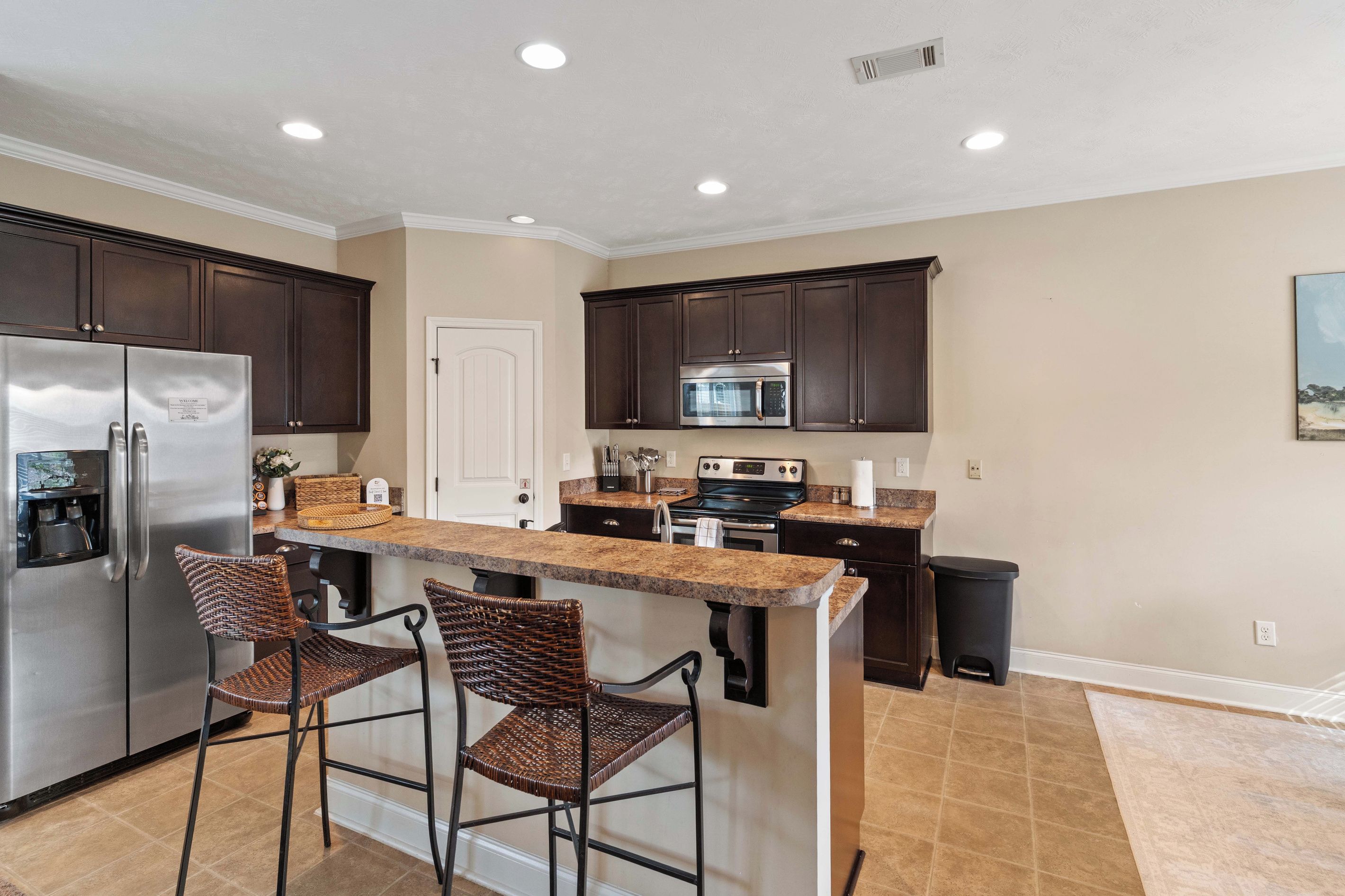 A modern kitchen with dark cabinetry, stainless steel appliances, and a central island with bar stools.