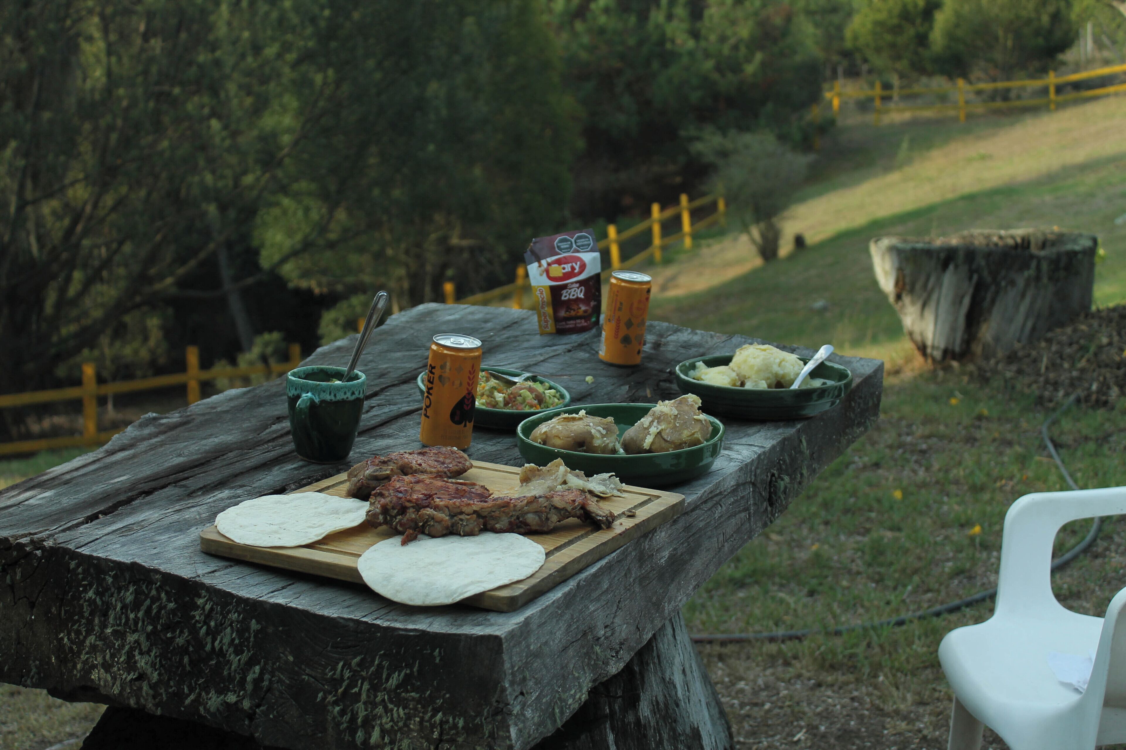 A picnic setup with food and drinks on a wooden table outdoors.