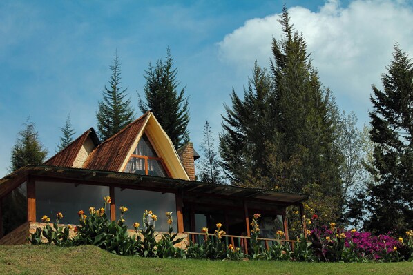 Una casa con techo inclinado, un porche y un jardín lleno de flores.
