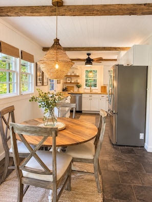 A kitchen with a round wooden table, chairs, a hanging light fixture, and a refrigerator.