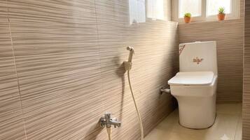 Une salle de bain avec des toilettes, une douche et une fenêtre agrémentée de plantes en pot.