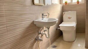 A bathroom with a sink, toilet, and a window with potted plants. - Classic Iubit Hotel (Kolkata)