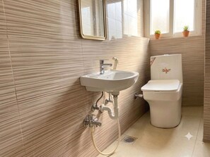 A bathroom with a sink, toilet, and a window with potted plants. - Classic Iubit Hotel (Kolkata)