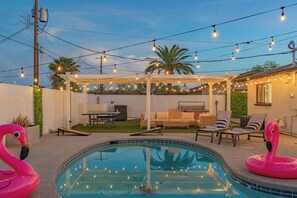 A backyard with a swimming pool, lounge chairs, a pergola with string lights, and a palm tree. - Heated Pool|Hot Tub|Ping Pong|Arcade|Pool table (Scottsdale)