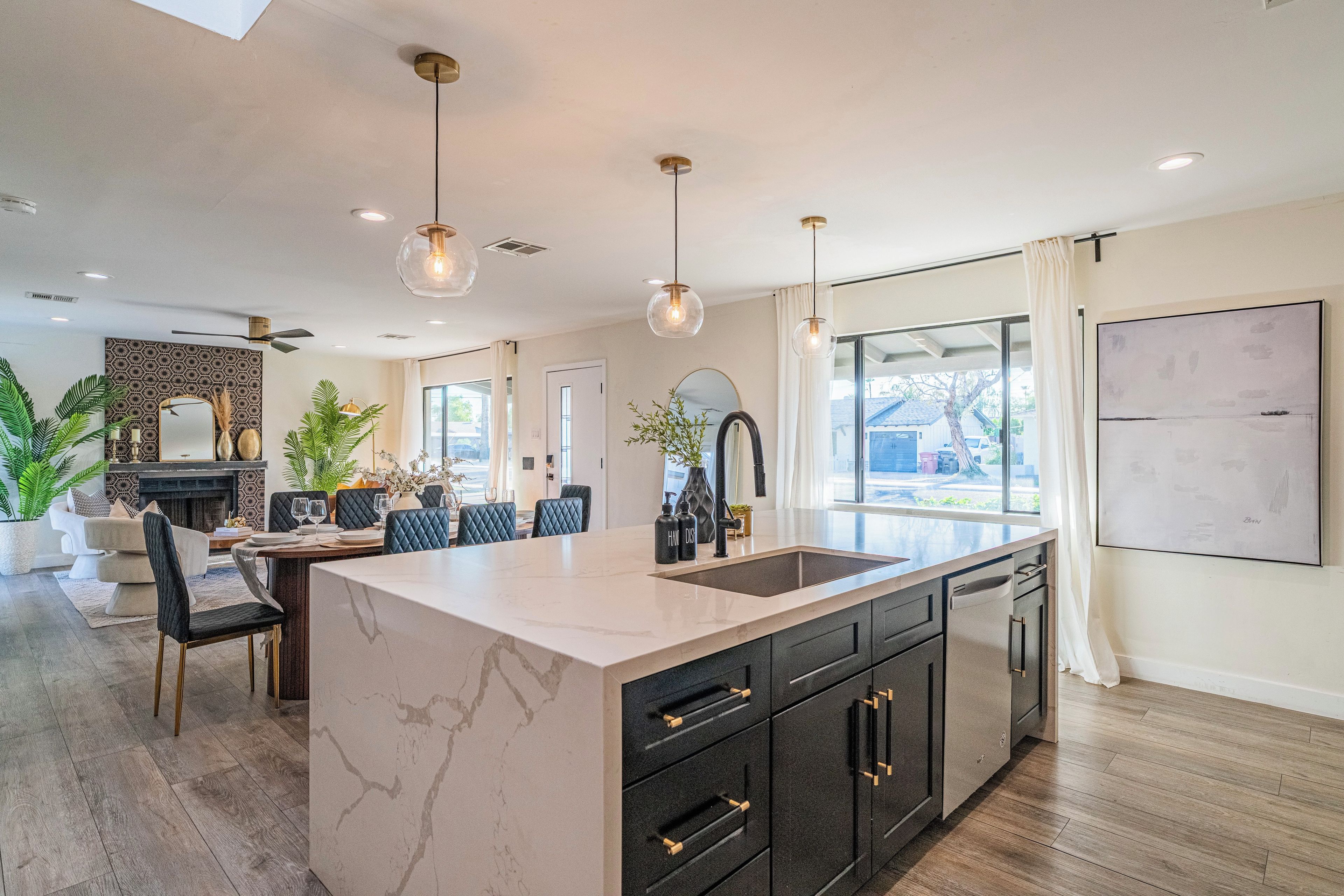 A modern kitchen with a marble island, black cabinetry, and pendant lighting.