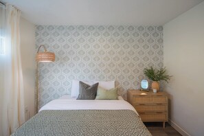 A bedroom with a patterned wallpaper, a bedside lamp, a bedside table with a mirror, and a potted plant. - Heated Pool|Hot Tub|Ping Pong|Arcade|Pool table (Scottsdale)