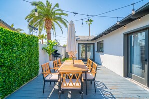 An outdoor patio with a wooden table and chairs, surrounded by a white wall and a green hedge. - Heated Pool|Hot Tub|Ping Pong|Arcade|Pool table (Scottsdale)