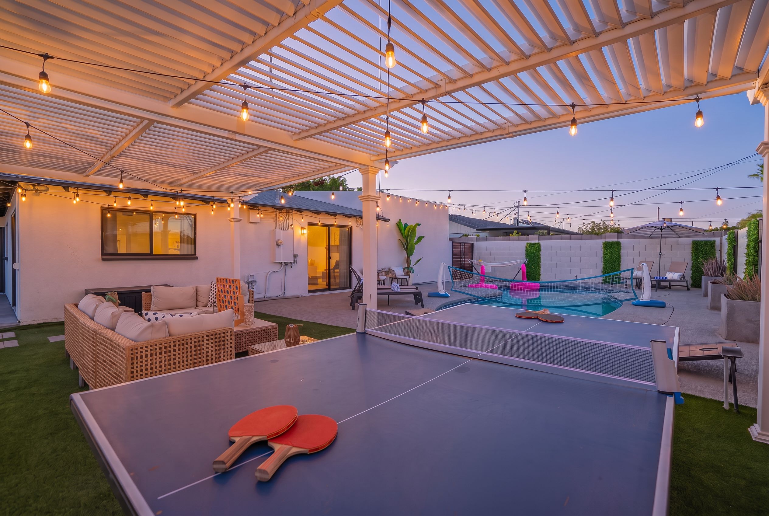 An outdoor recreational area with a ping pong table, seating, and a pool.