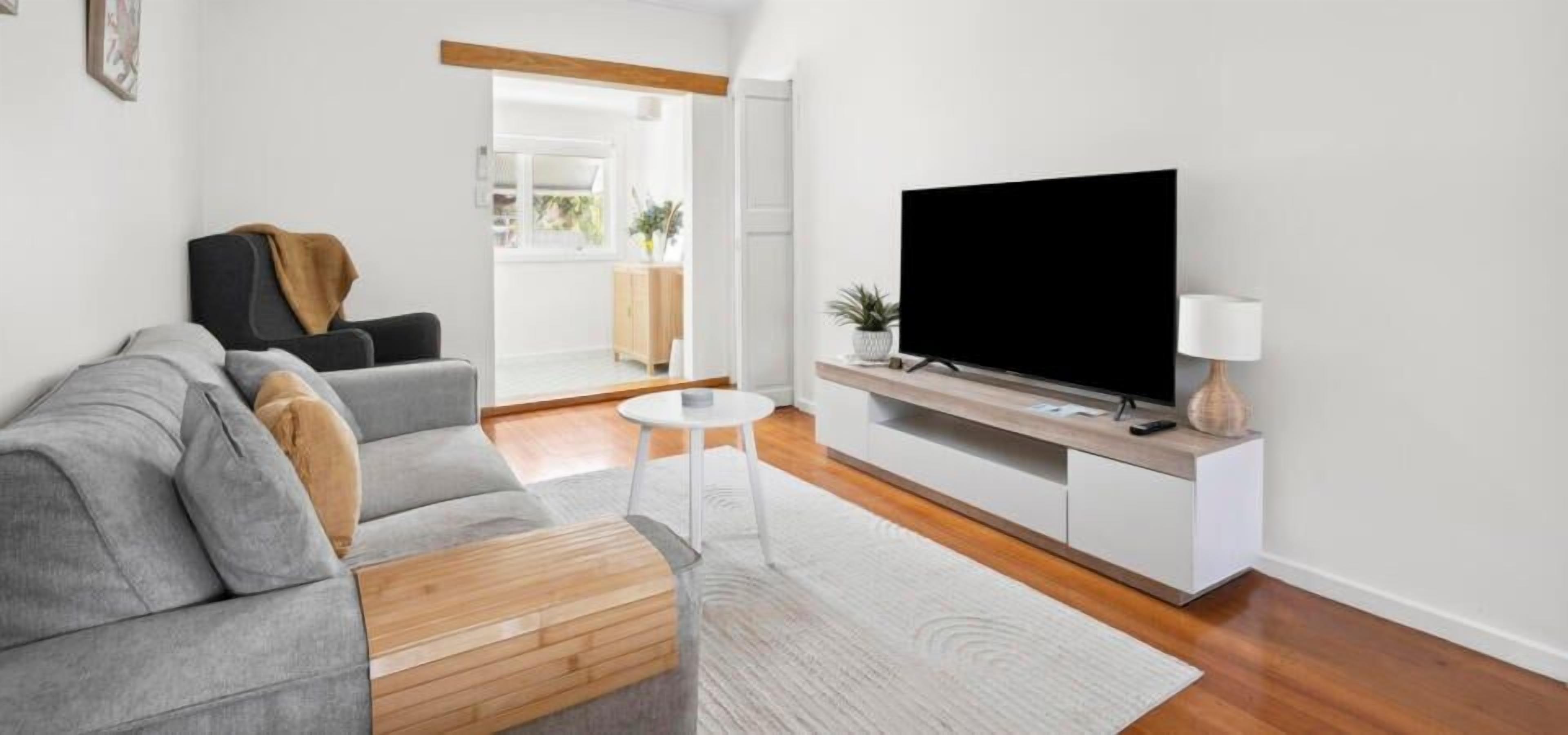 Een moderne woonkamer met een grijze bank, een flatscreen televisie en een klein wit tafeltje.