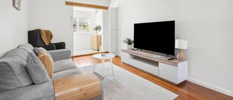 Un soggiorno moderno con un divano grigio, una TV a schermo piatto e un piccolo tavolino bianco.