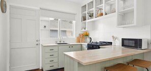 Una cucina con mobili bianchi, un piano di lavoro in legno, un fornello e un forno a microonde.