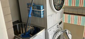 A laundry area with a washing machine, a metal basin, and detergent boxes. - Cosy Geelong West Townhouse with Secure Garage (Greater Geelong)