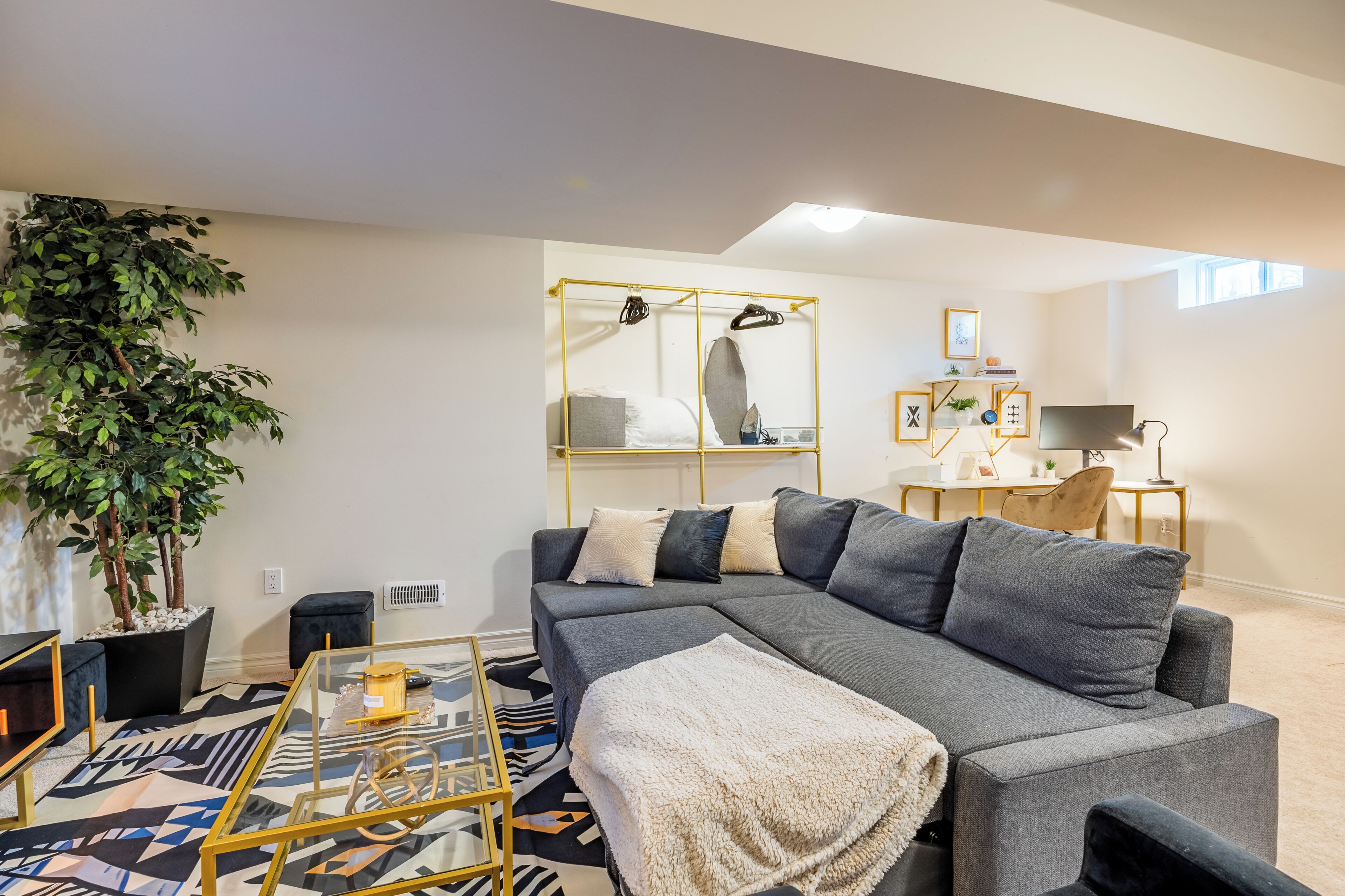 A modern living room with a sectional sofa, a glass coffee table, a potted plant, and a small desk with a lamp.