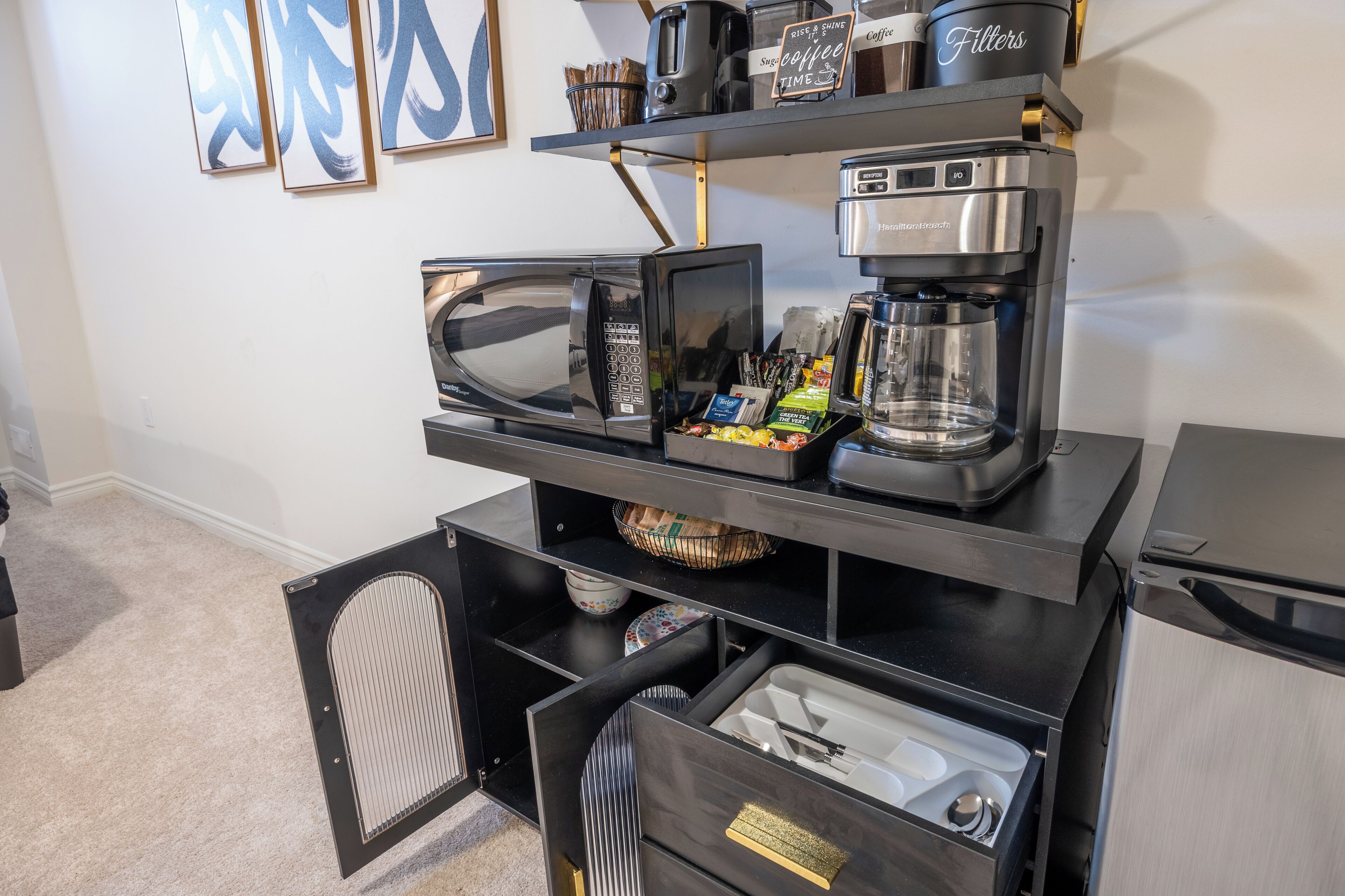 Une petite cuisine équipée d’un four à micro-ondes, d’une machine à café et de tiroirs de rangement.