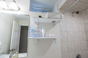 Un bagno con lavandino bianco, uno specchio, zona doccia e uno scaffale con articoli da toilette.
