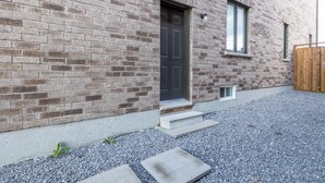 Un bâtiment en briques avec une porte sombre, une petite fenêtre et une clôture en bois.