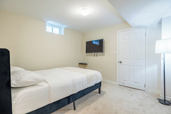 A bedroom with a bed, a television mounted on the wall, a door, and a lamp.