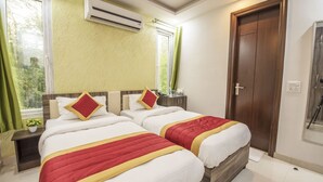 A hotel room with two beds, a wooden wardrobe, a window with curtains, an air conditioning unit, and a door. - Comfort Home Stay (New Delhi)