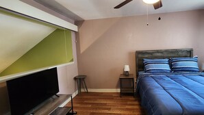 A bedroom with a bed, a nightstand, a lamp, a television, and a ceiling fan.