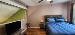 Ein Schlafzimmer mit einem Bett, einem Nachttisch, einer Lampe, einem Fernseher und einem Deckenventilator.