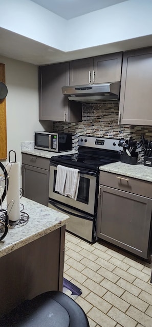 Cocina compacta con microondas, estufa, horno y una pequeña isla con pileta.