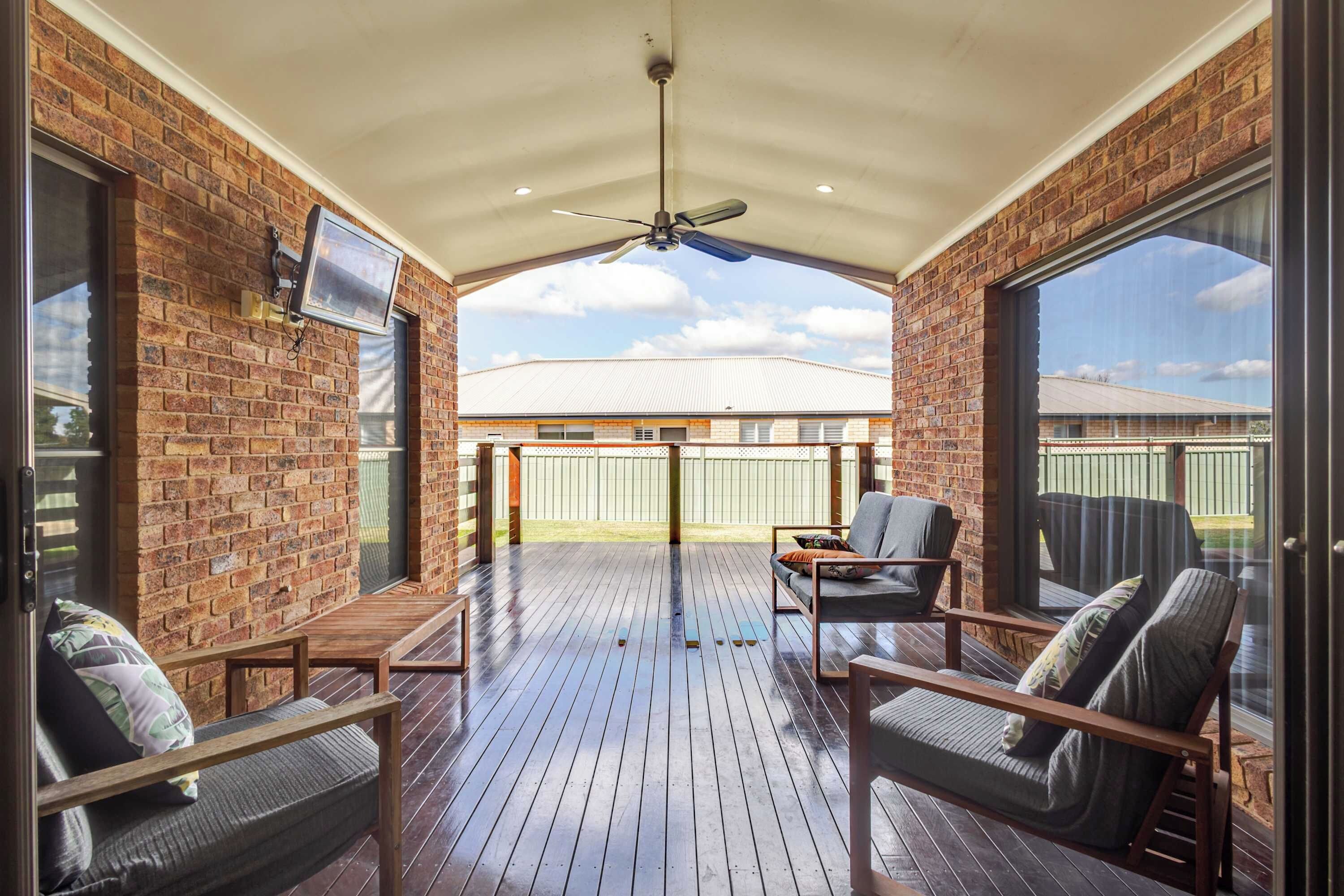 A covered patio with brick walls, a ceiling fan, and a view of a house in the background.