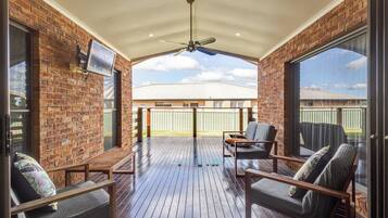 A covered patio with brick walls, a ceiling fan, and a view of a house in the background.