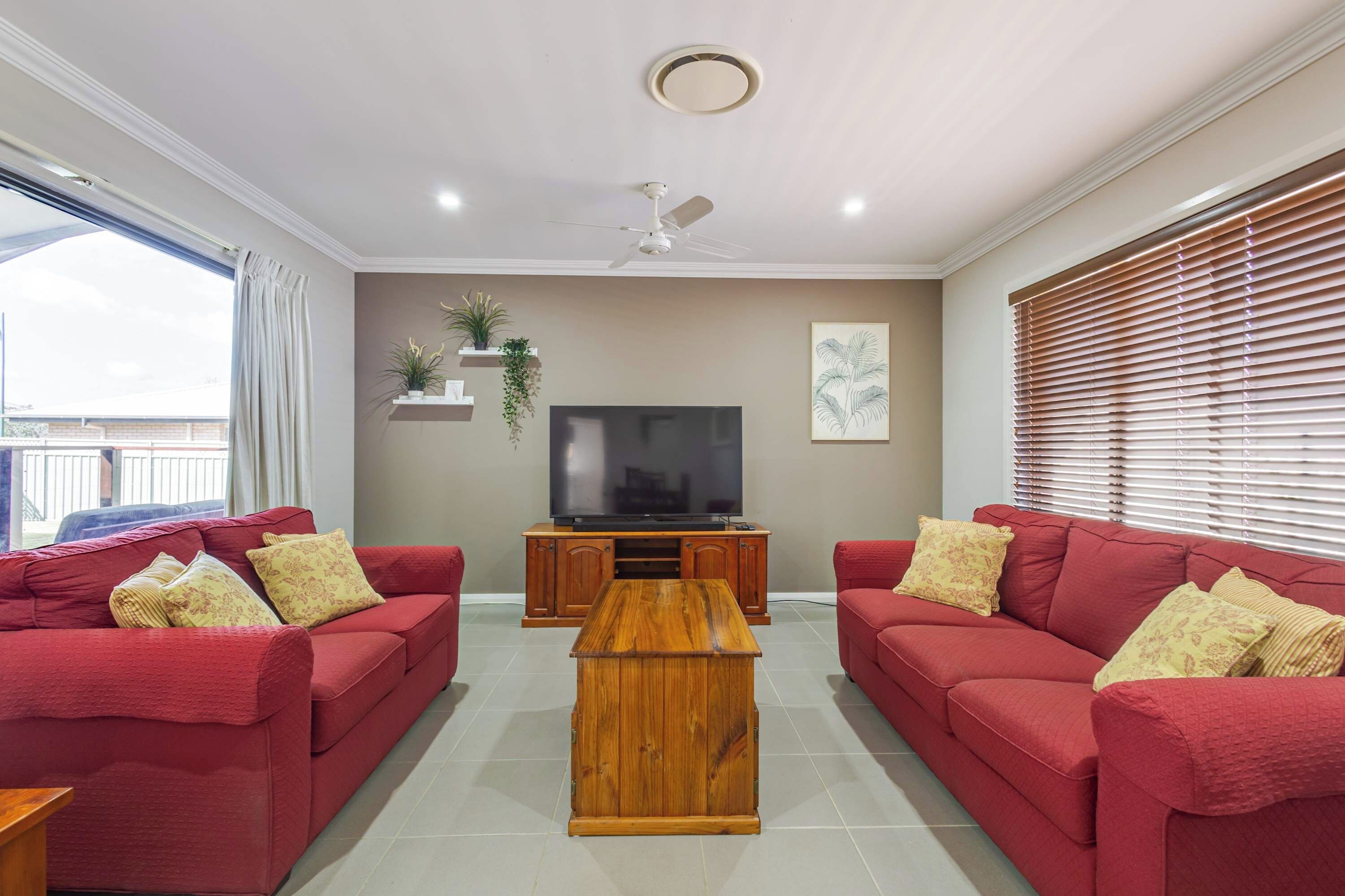 A living room with two red sofas, a wooden coffee table, a TV on a wooden stand, and a ceiling fan.