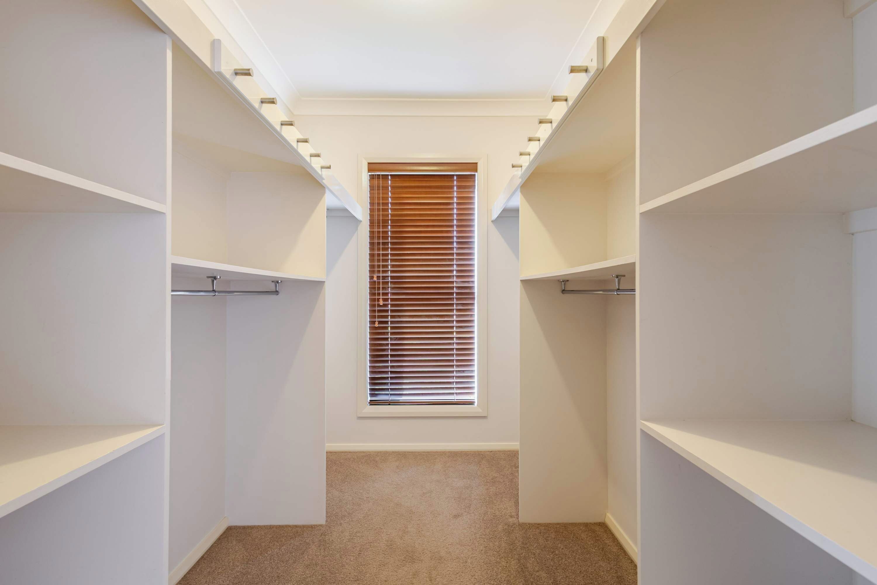 Ein begehbarer Kleiderschrank mit Einbauregalen und einem Fenster mit Jalousien.