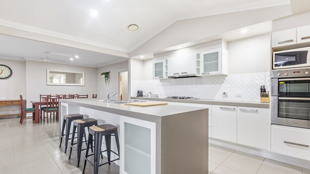 A modern kitchen with a central island, bar stools, a dining area with a wooden table and chairs, and a built-in oven. - The Ritz, Family Pool Home, Dubbo (Dubbo)