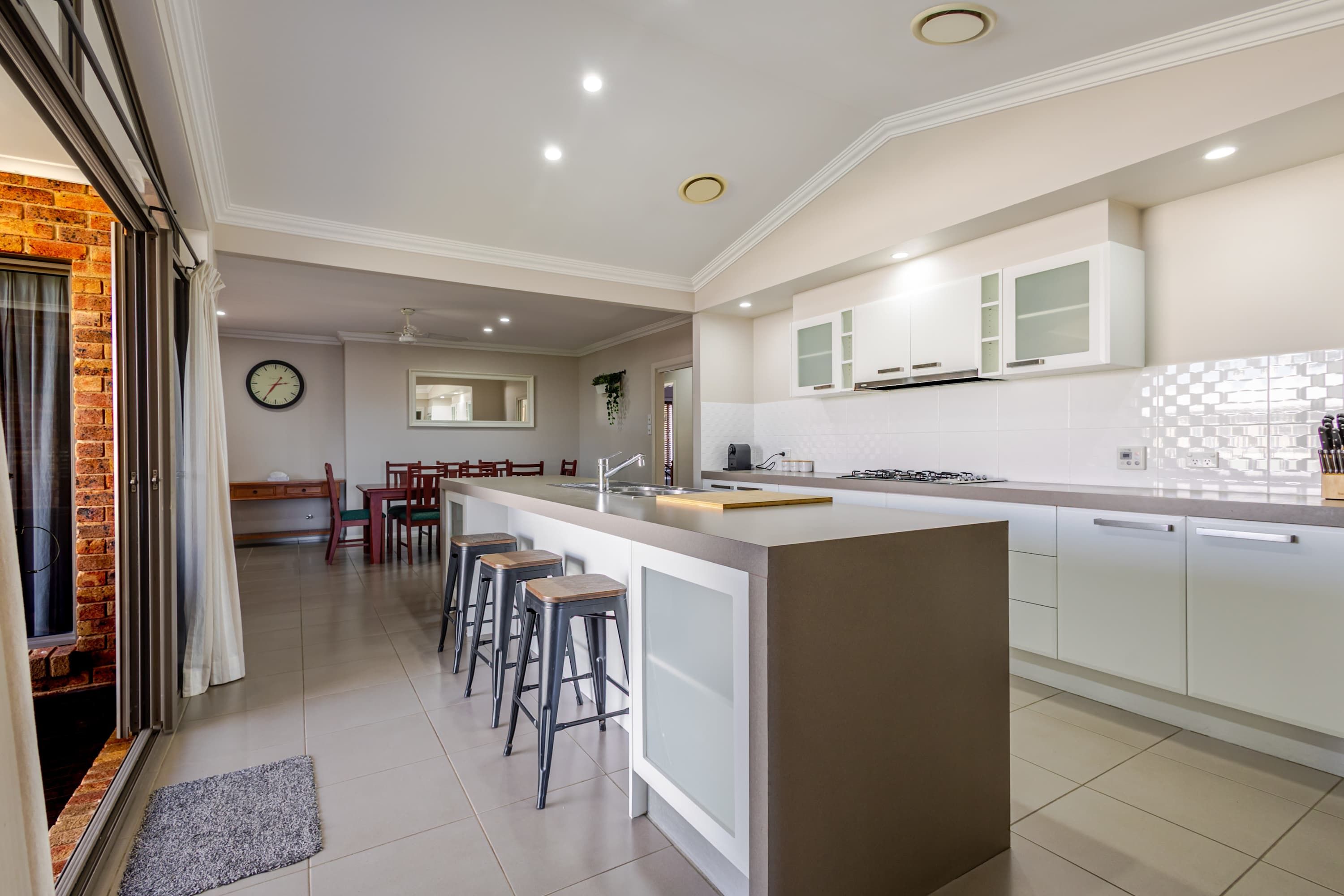 A modern kitchen with a central island, bar stools, and a dining area with a table and chairs.