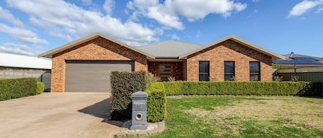 Une maison à deux étages, construite en briques, avec un garage, une pelouse bien entretenue et une boîte aux lettres.