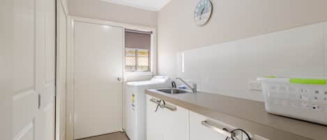 Una cocina con lavadora, un lavabo y un reloj en la pared.