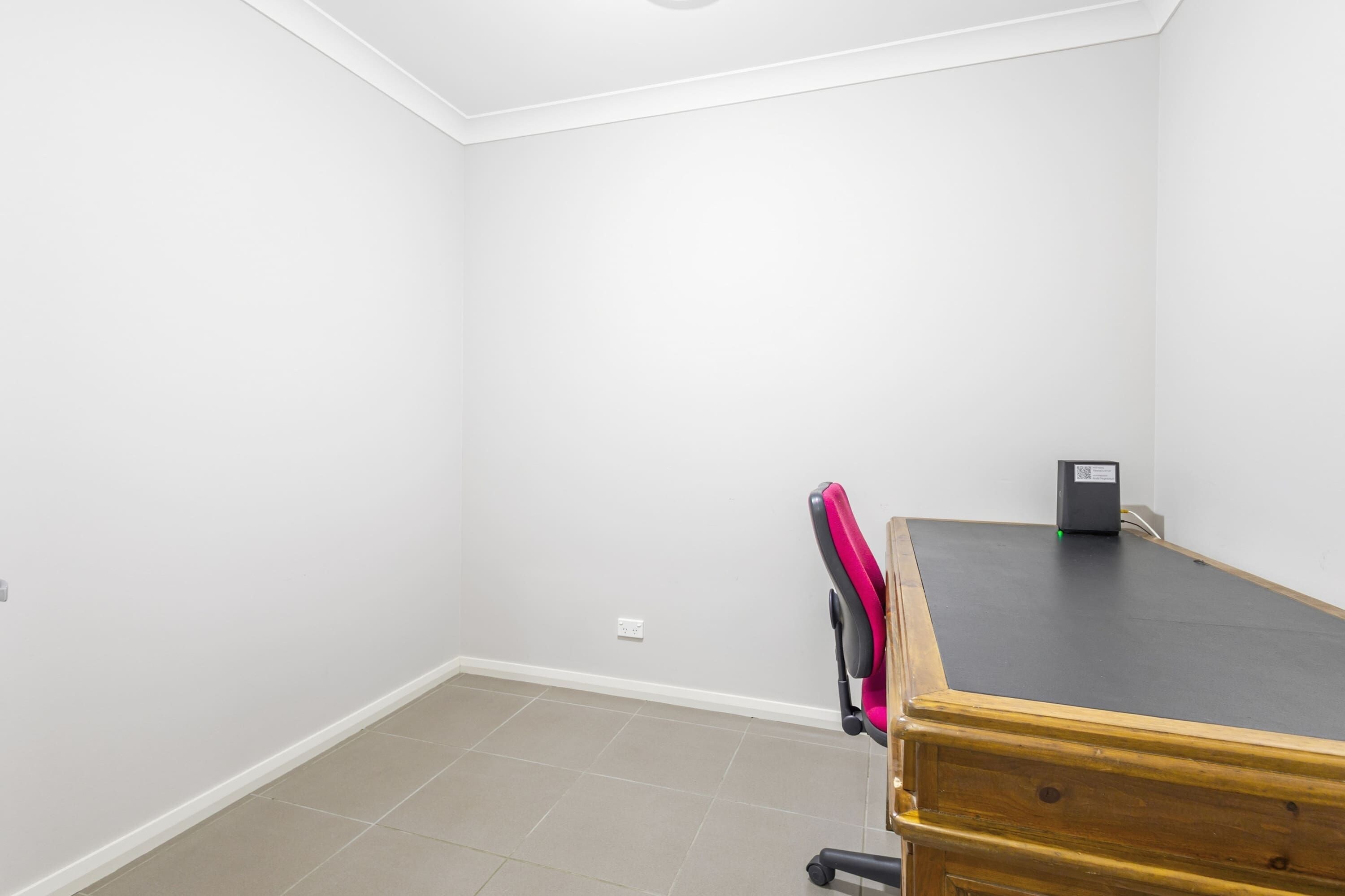 A room with a wooden desk, a chair, and a small black object on the desk.