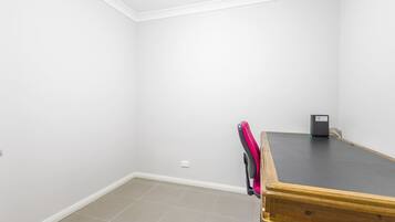 A room with a wooden desk, a chair, and a small black object on the desk.
