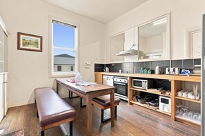 A compact kitchen with a wooden table, bench, and built-in appliances including a microwave, oven, and toaster. - Edinburgh - Queen Room + Free Parking (Hobart)