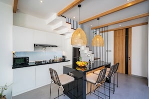 A modern kitchen with a central island, black bar stools, and a dining table. - Villa Scorpia 4 Bingin (Pecatu)