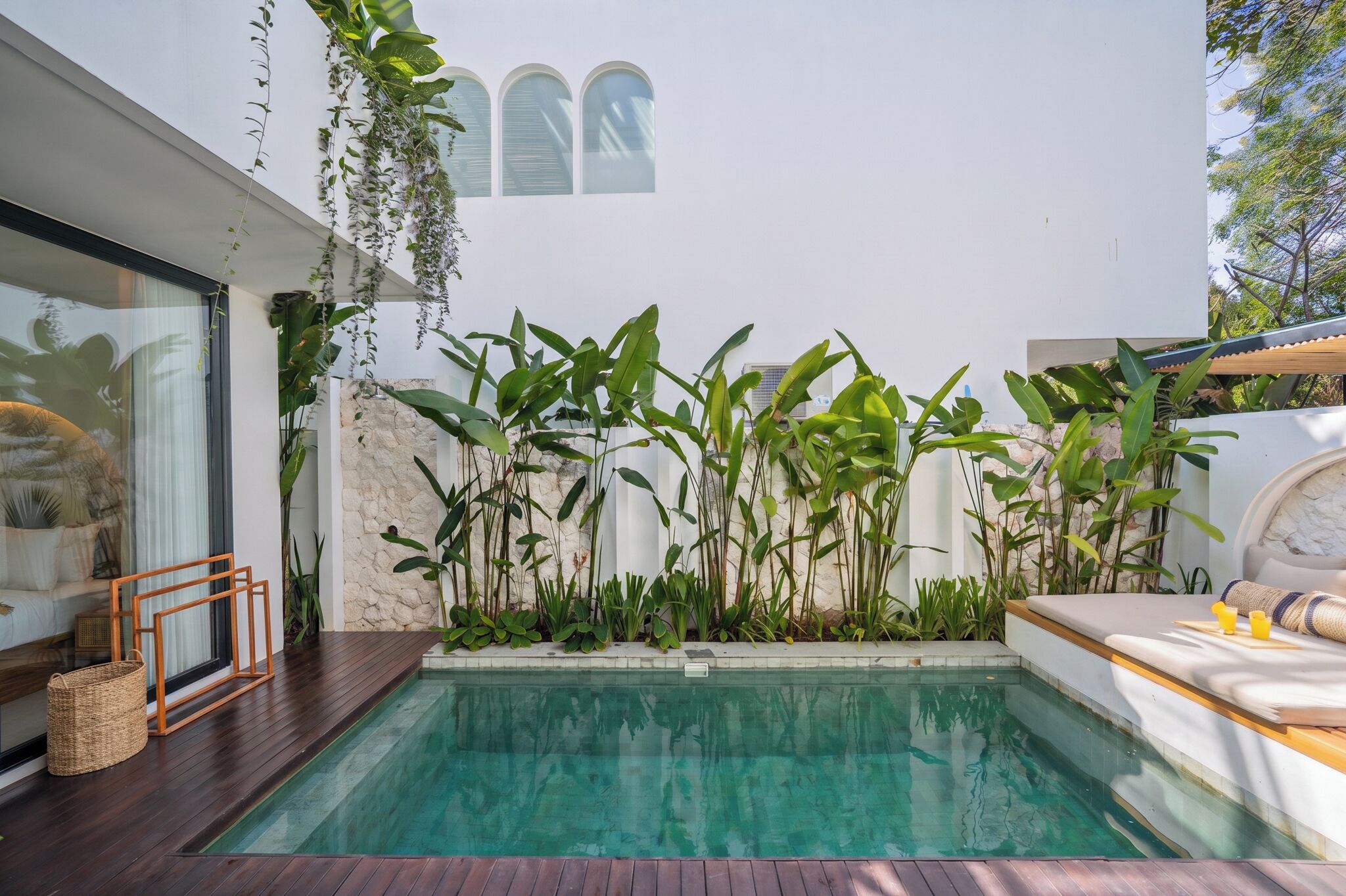 A modern outdoor pool area with a stone wall, lush greenery, and a wooden deck.
