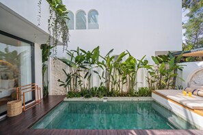 A modern outdoor pool area with a stone wall, lush greenery, and a wooden deck. - Villa Scorpia 4 Bingin (Pecatu)