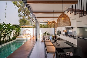 A modern kitchen with a built-in island, stainless steel appliances, and a dining area with bar stools. - Villa Scorpia 4 Bingin (Pecatu)