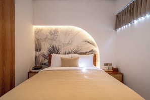 A neatly made bed with a headboard featuring a leaf pattern, a bedside table with a lamp, and a wall-mounted curtain. - Villa Scorpia 4 Bingin (Pecatu)