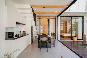 A modern kitchen with a dining area, a staircase, and a view of a bedroom. - Villa Scorpia 4 Bingin (Pecatu)