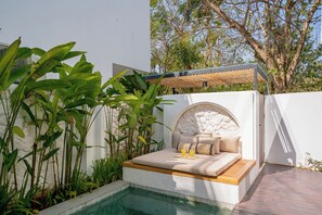 A modern outdoor seating area with a pool, surrounded by lush greenery and a stone wall. - Villa Scorpia 4 Bingin (Pecatu)