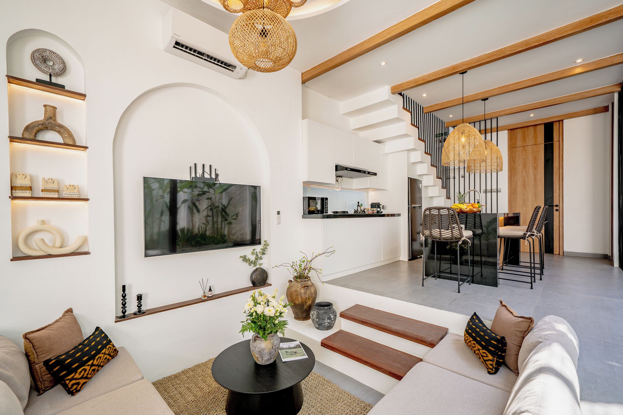 A modern living room with a flat-screen TV, a dining area with a staircase, and a kitchen with a built-in oven.