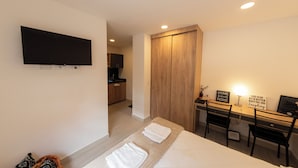 A hotel room with a bed, a desk with a chair, a TV mounted on the wall, and a wooden wardrobe. - Punto Chapinero - Zona Gourmet (Bogotá)