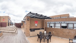 An outdoor patio area with a brick wall, a pergola, a grill, and a table with chairs. - Punto Chapinero - Zona Gourmet (Bogotá)
