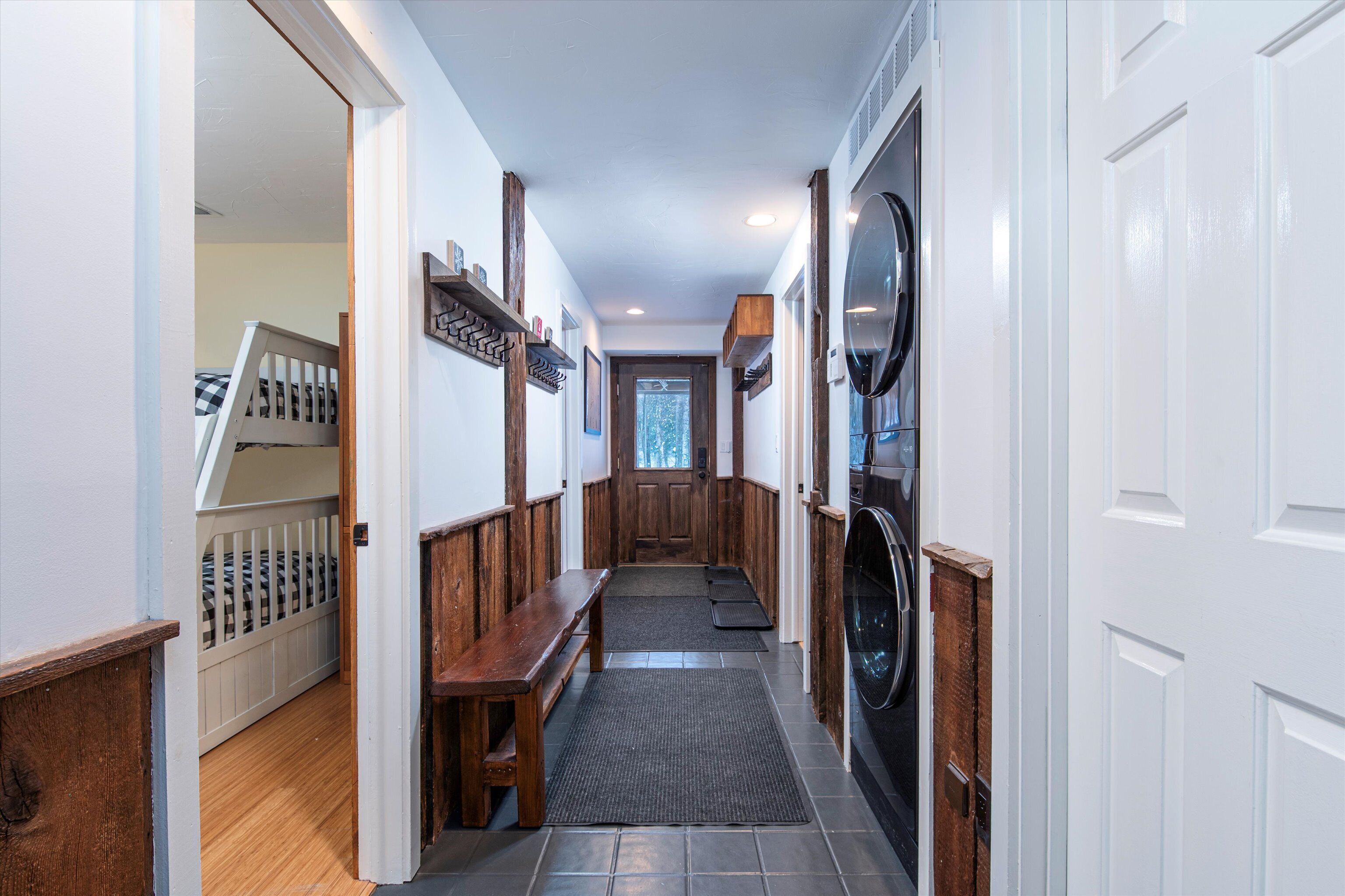 A hallway with a wooden bench, a coat rack, and a door leading to a room with a large mirror.